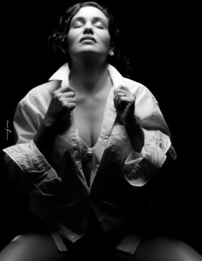 Mulher em ensaio fotográfico feminino em estúdio, com iluminação dramática em preto e branco, expressando confiança e introspecção.